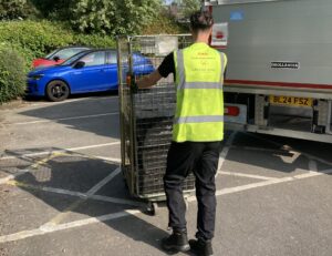 member of GXO staff wearing GXO high vis top pushing trolley to back of lorry